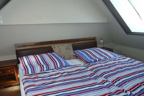 Ein Schlafzimmer mit schrägen Wänden, einem hölzernen Kopfteil, einem Bett mit gestreifter Bettwäsche und einem Nachttisch mit einer Lampe.
