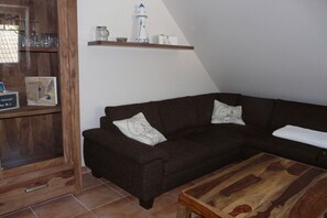 Ein dunkelbraunes Sofa mit zwei Kissen, ein Holztisch, eine Ablage mit Glaswaren und einem Leuchtturmmodell, sowie ein gerahmtes Zertifikat links.