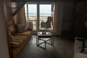 A living room with a sofa, a coffee table, and a view of the city through large windows. - Holiday apartment with 1 bedroom (Waren \/ Müritz)