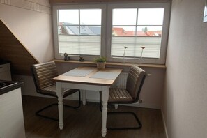 Una cocina pequeña con una mesa y dos sillas, una ventana con persianas y un radiador.