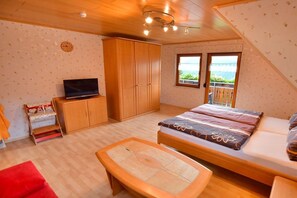 A bedroom with a bed, a TV, a wardrobe, and a balcony with a view. - Holiday apartment with 2 bedrooms (Oppenau)