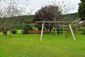 Un espacio al aire libre con césped, un columpio de madera, un banco y una pequeña construcción.