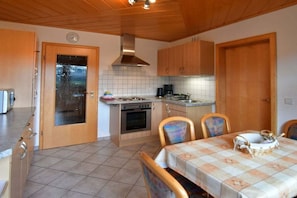A compact kitchen with a stove, oven, and wooden cabinets. There is a dining table with chairs and a basket on it. - Holiday apartment with 2 bedrooms (Oppenau)