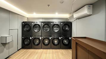 A laundry room with multiple washing machines, a wooden floor, and a built-in bench.