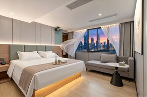 Een moderne hotelkamer met een groot bed, een bank, een klein tafeltje en uitzicht op de stad.