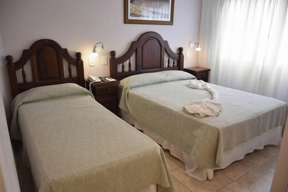 A hotel room with two single beds, a wooden headboard, bedside lamps, a telephone, and a framed picture on the wall.