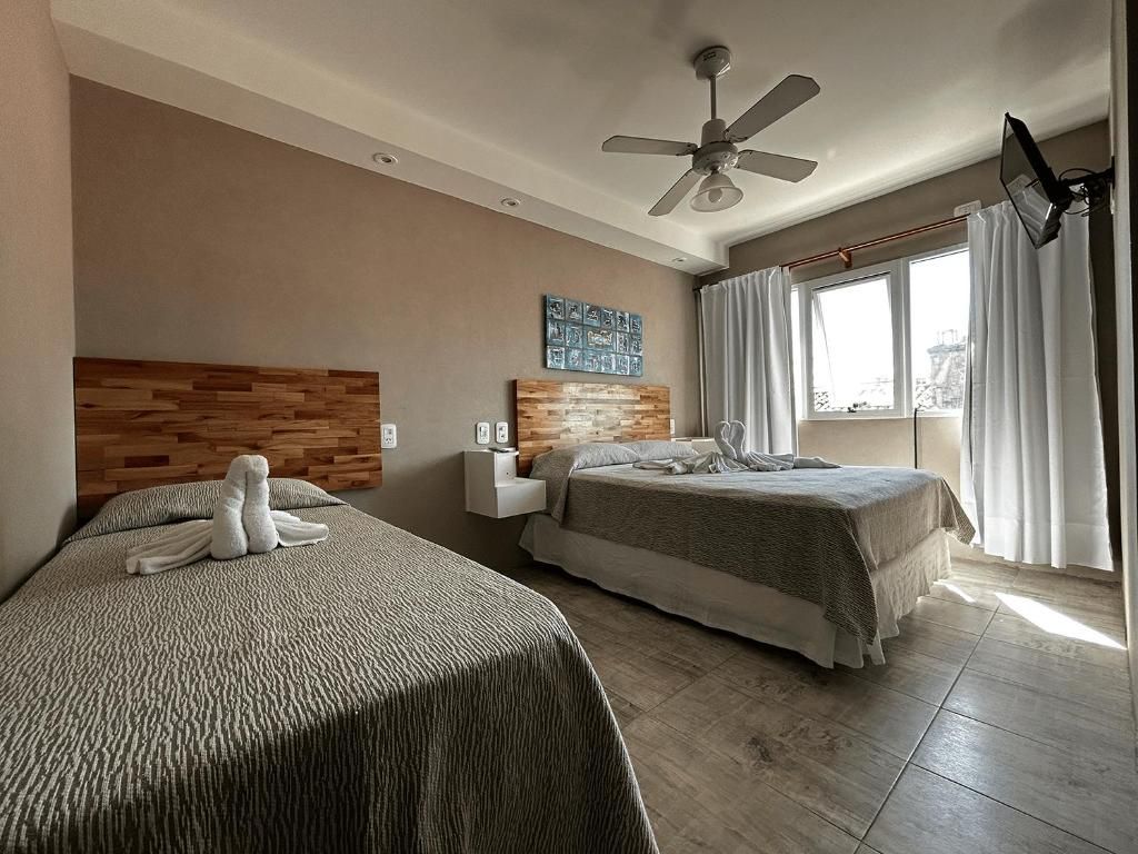 A hotel room with two beds, a ceiling fan, a window with curtains, and a wall-mounted TV.