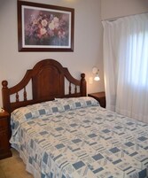 Un dormitorio con cabecera de madera, colcha estampada, una obra de arte floral enmarcada en la pared y una lámpara de noche.