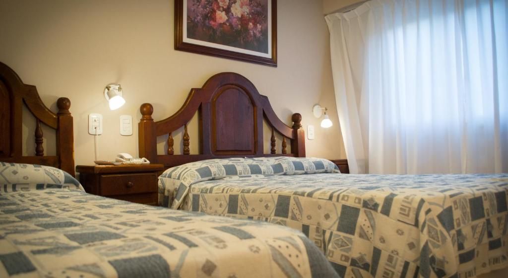 A hotel room with two beds, a nightstand with a telephone, wall-mounted lamps, and a painting on the wall.