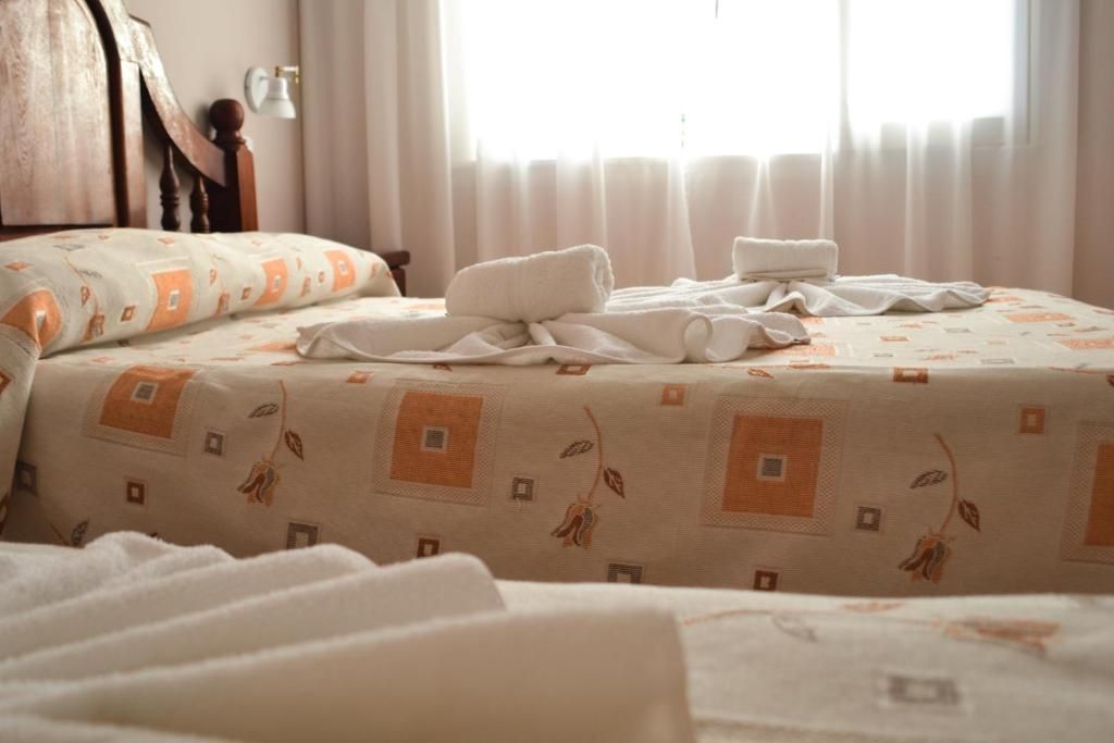 Un lit bien fait, avec une couvre-lit à motifs et des serviettes, une tête de lit en bois et une fenêtre avec des rideaux.