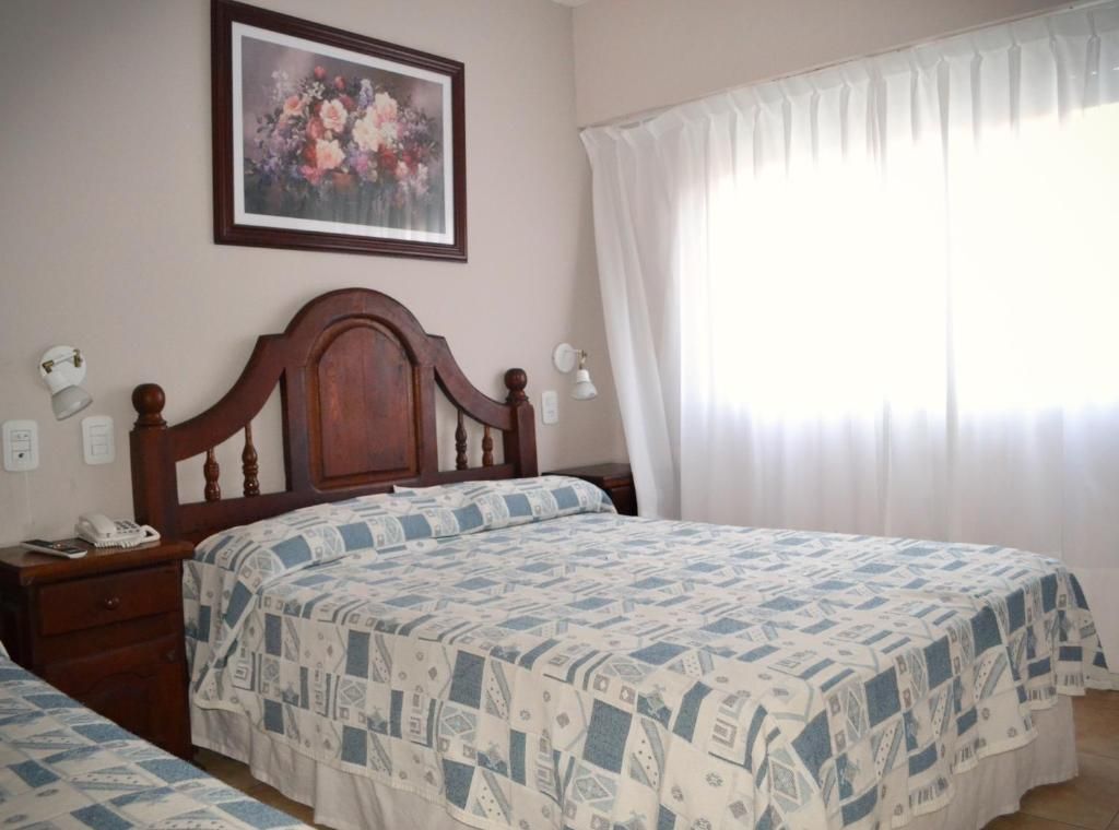Un dormitorio con una cama de madera, una mesita de noche con lámpara y un cuadro con flores en la pared.