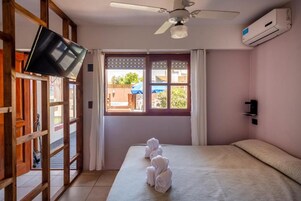Una habitación con cama, ventilador de techo, equipo de aire acondicionado y ventana con cortinas.