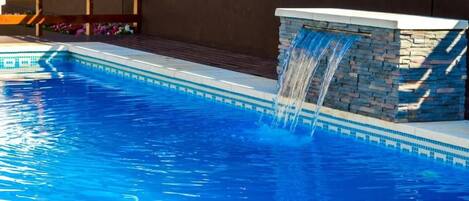 En swimmingpool med ett vattenfall och en stenmur.