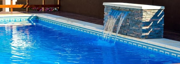 A swimming pool with a waterfall feature and a stone wall. - Hotel Rideamus (Villa Gesell)
