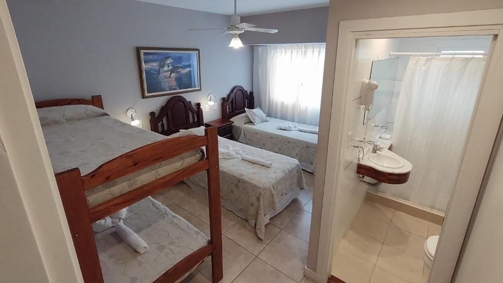 Un dormitorio con dos camas, ventilador de techo, un cuadro, y un baño con ducha e inodoro.