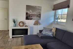 A living room with a sofa, a lamp, a painting, and a window with a view. - Holiday apartment Bug (Dranske)