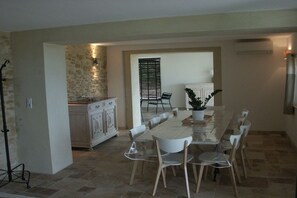 A dining area with a long table, chairs, a potted plant, and a kitchen in the background. - Holiday home with 5 bedrooms (Bagnols sur Cèze)