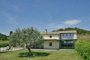 Una casa a due piani con un'ampia porta d'ingresso in vetro, un piccolo balcone e un albero nel cortile.
