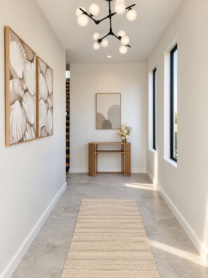 A hallway with a modern light fixture, a console table with a vase, and two framed artworks on the walls. - The Brighton Edit | 5BR Coastal Escape (South Brighton)