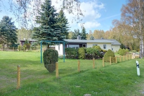 A residential property with a fenced yard, a large coniferous tree, and a house with a sloped roof. - Holiday home with 1 bedroom (Marienberg\/OT Rittersberg)