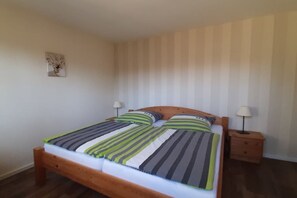 Un lit simple avec une tête de lit en bois, deux tables de chevet avec des lampes, un tableau accroché au mur et une couvre-lit à rayures.