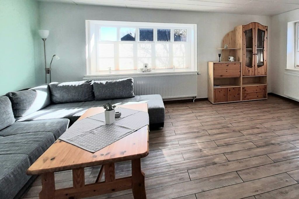 Une pièce avec un canapé gris, une table basse en bois, un meuble en bois et un radiateur.
