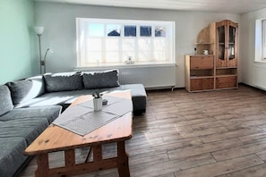 Ein Zimmer mit einer grauen Couch, einem Holztisch, einem Holzschrank und einer Heizung.