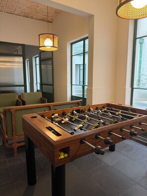 Ein Tischkicker in einem Raum mit Ziegeldecke, großen Fenstern und einer Hängeleuchte.