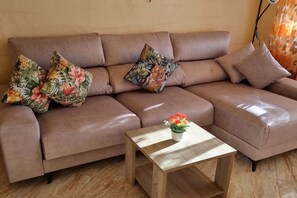 A brown leather sofa with floral cushions and a small wooden coffee table with a flower vase. - Casa Denise with fiber optic internet (Costa Calma)
