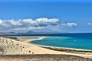 A coastal landscape with a sandy beach, calm sea, and distant mountains under a partly cloudy sky. - Casa Denise with fiber optic internet (Costa Calma)