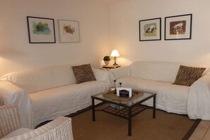 A living room with a white sofa, a glass coffee table, and a lamp. There are framed pictures on the wall. - Holiday home in Gruissan with swimming pool (Gruissan)