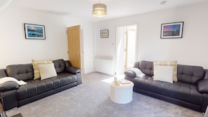 A living room with two black leather sofas, a white coffee table, and framed pictures on the walls. - Mullingarroch Mill — Historic Mill House on the River Spey, Sleeps 6 (Boat of Garten)