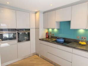 A modern kitchen with white cabinetry, a built-in oven, and a blue countertop. - Mullingarroch Mill — Historic Mill House on the River Spey, Sleeps 6 (Boat of Garten)