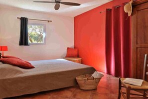 Ein Schlafzimmer mit einem Bett, einem Fenster, einem Deckenventilator, einer roten Wand und einer Holztür.