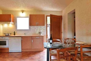 Cozinha compacta com armários de madeira, lava-louças e área de jantar com mesa e cadeiras.