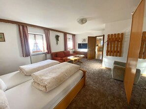 Ein Hotelzimmer mit zwei Betten, einem Schlafsofa, einem kleinen Tisch und einem Fernseher.