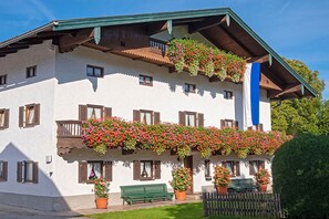 Ein mehrstöckiges Gebäude mit Balkonen, die mit Blumen geschmückt sind, einer blauen Flagge und einer grünen Bank.