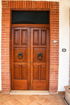 A double wooden door with two round metal knockers, set in a brick wall with a white door frame. - Cetine Vecchie Farmstay – Il Giglio (Torrita di Siena)
