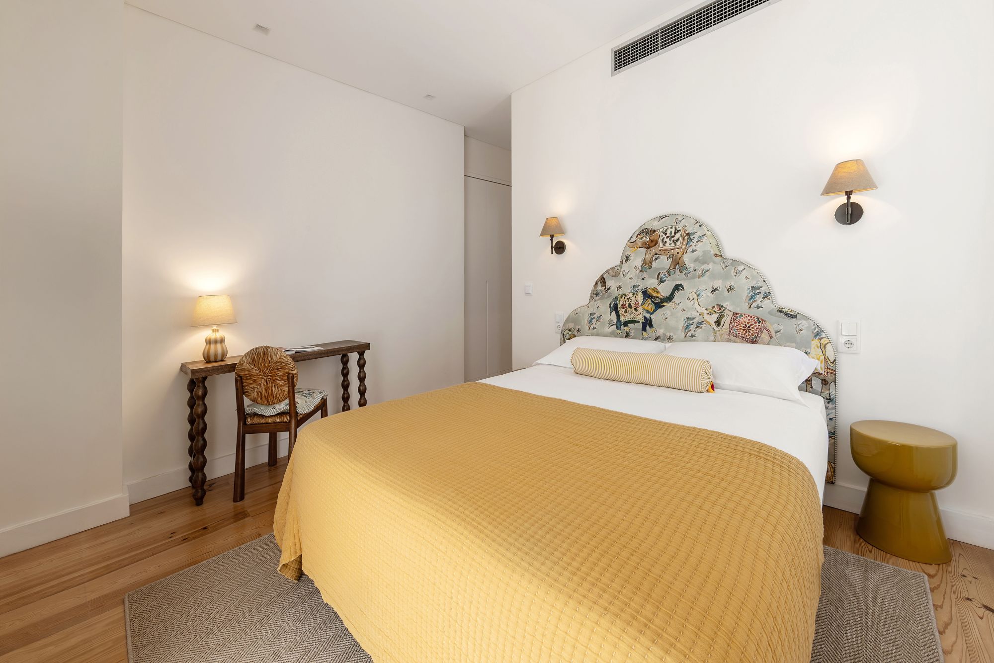 Ein Schlafzimmer mit einem Bett, Nachttischlampen, einem Sessel, einem kleinen Tisch und einem dekorativen Kopfteil.