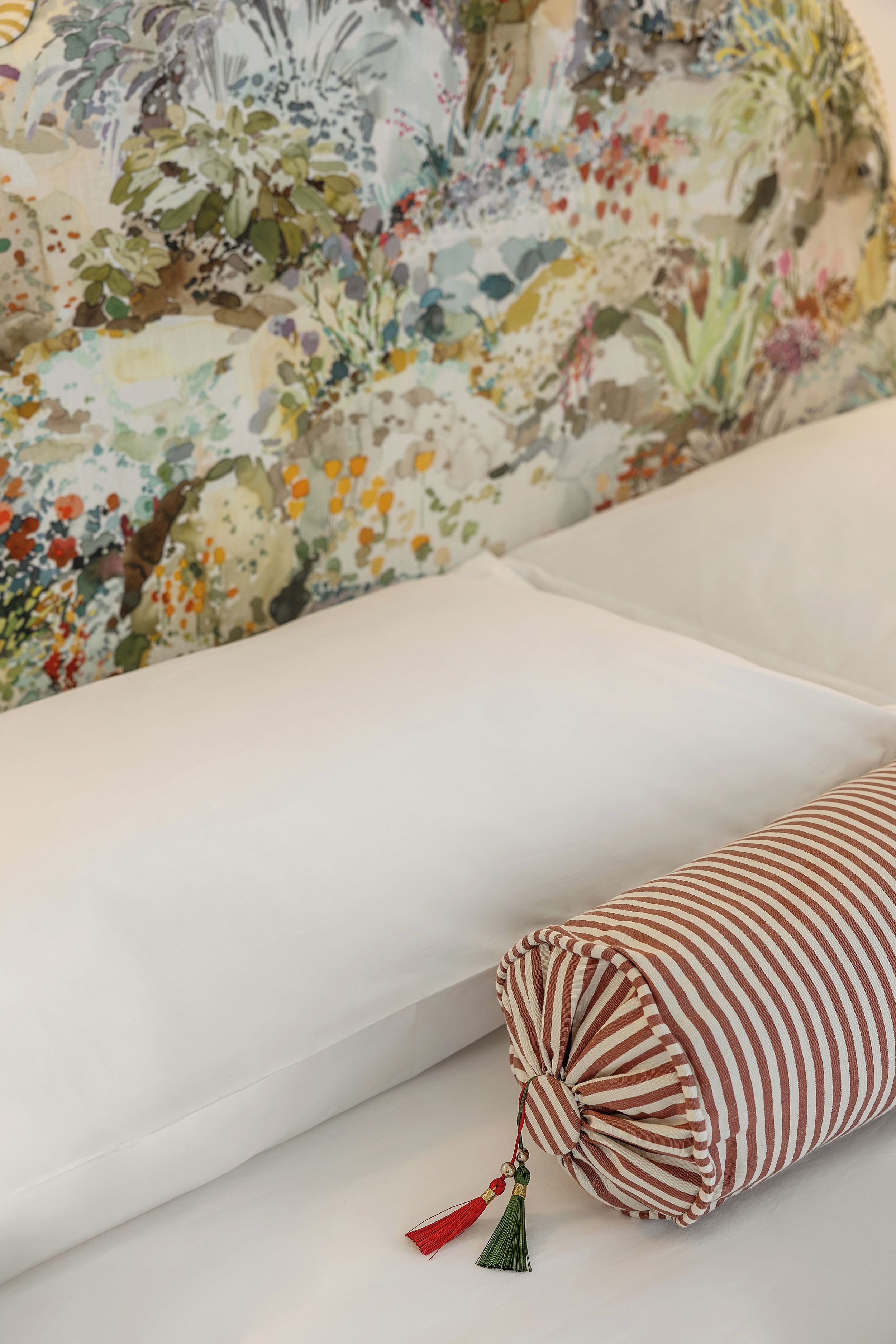 A bed with a white sheet and a striped pillow with tassels.