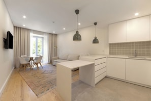 Uma cozinha moderna com armários brancos, um espaço de refeições com mesa e cadeiras, e uma sala de estar com sofá.