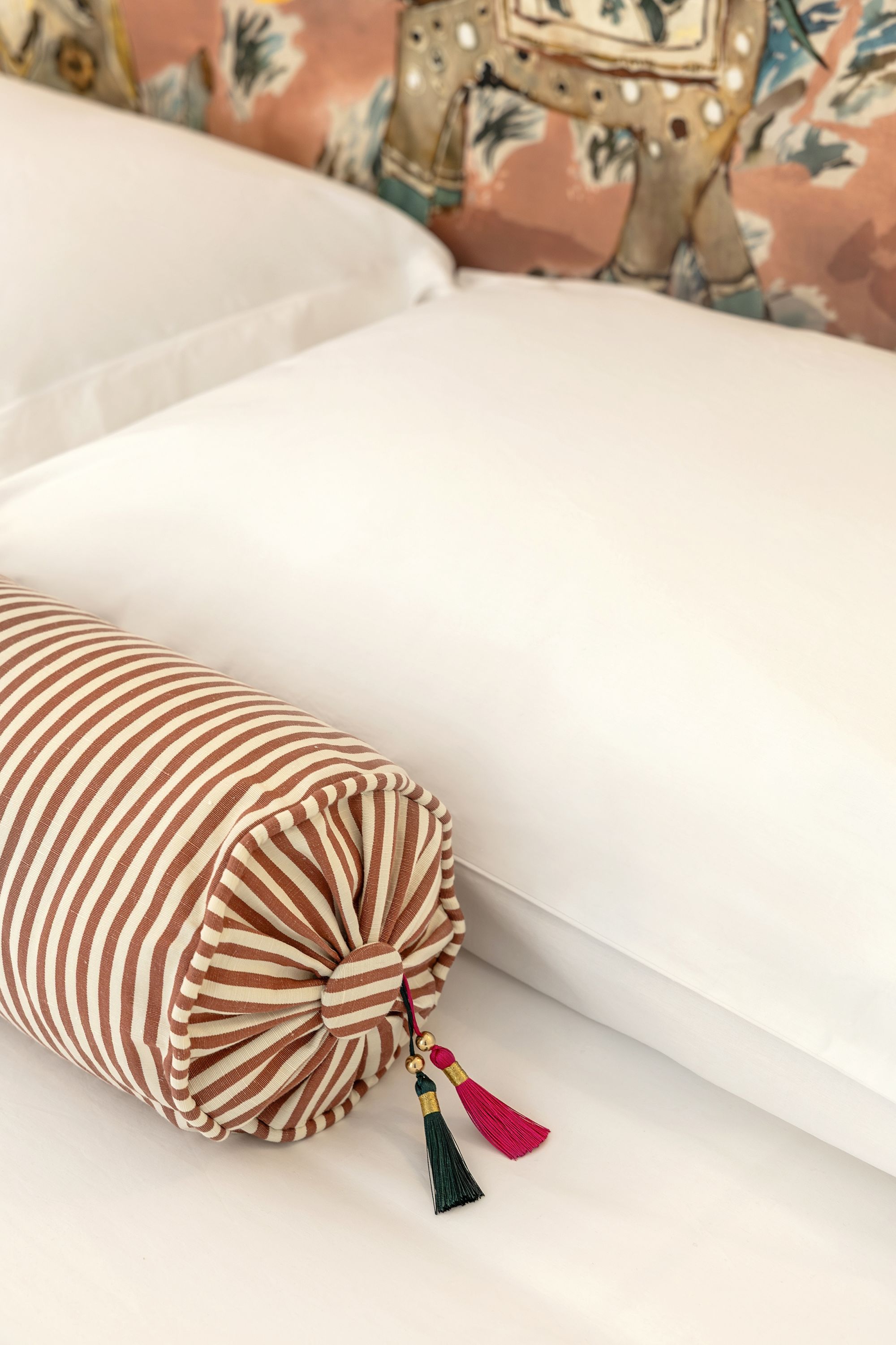 A bed with white sheets and a striped pillow with tassels.