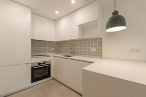 Cozinha moderna com armários brancos, forno embutido, pia e luminária pendente.