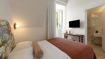 A hotel room with a bed, a television, a desk with a lamp, and a bathroom visible through an open door.
