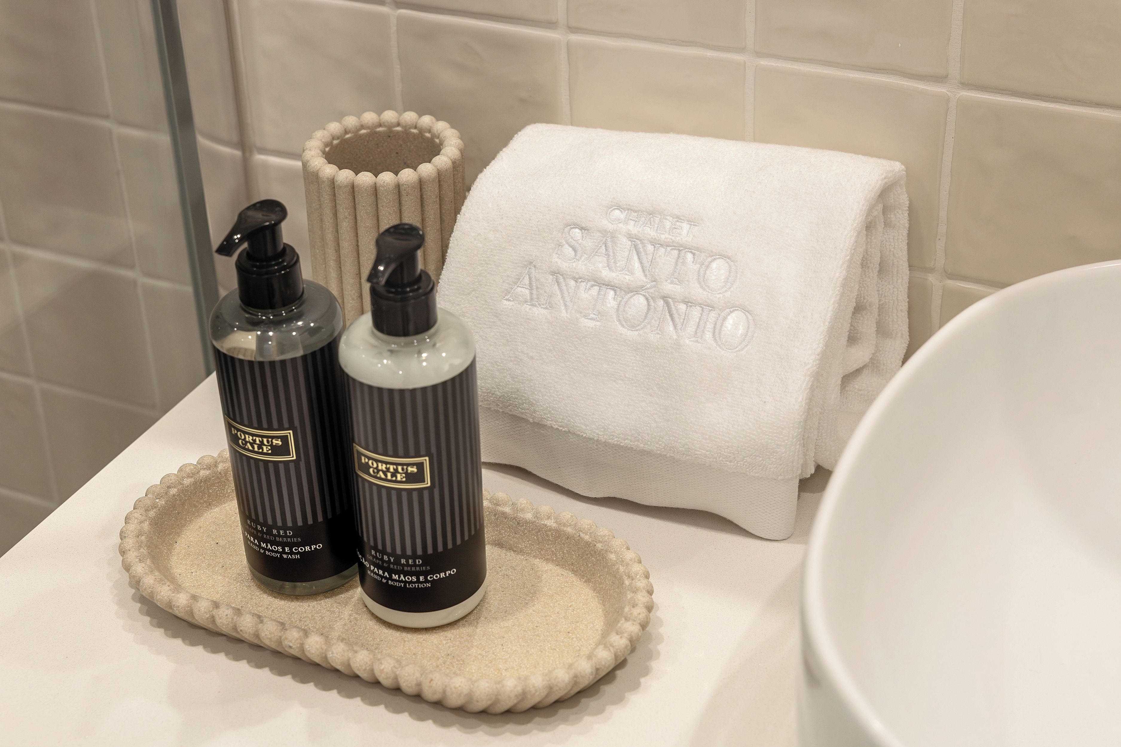 A bathroom with a white towel, two bottles of Portus Calle body wash, and a white basin.