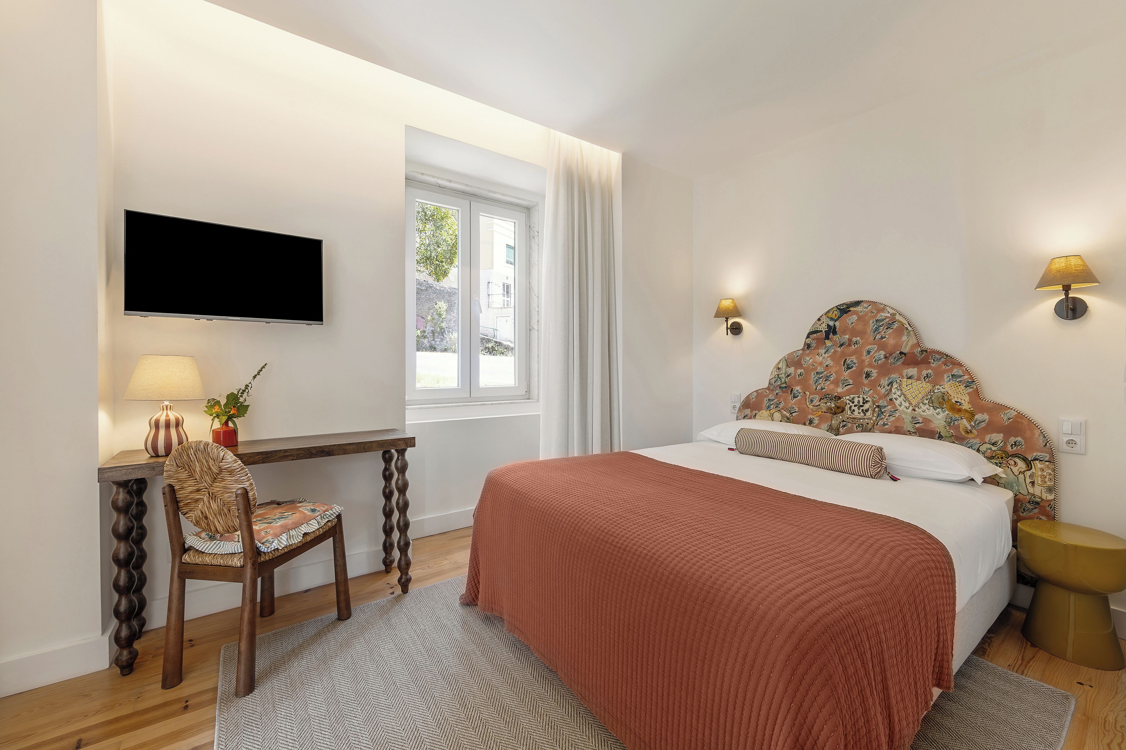 A hotel room with a bed, a desk with a chair, a television, and a window with curtains.