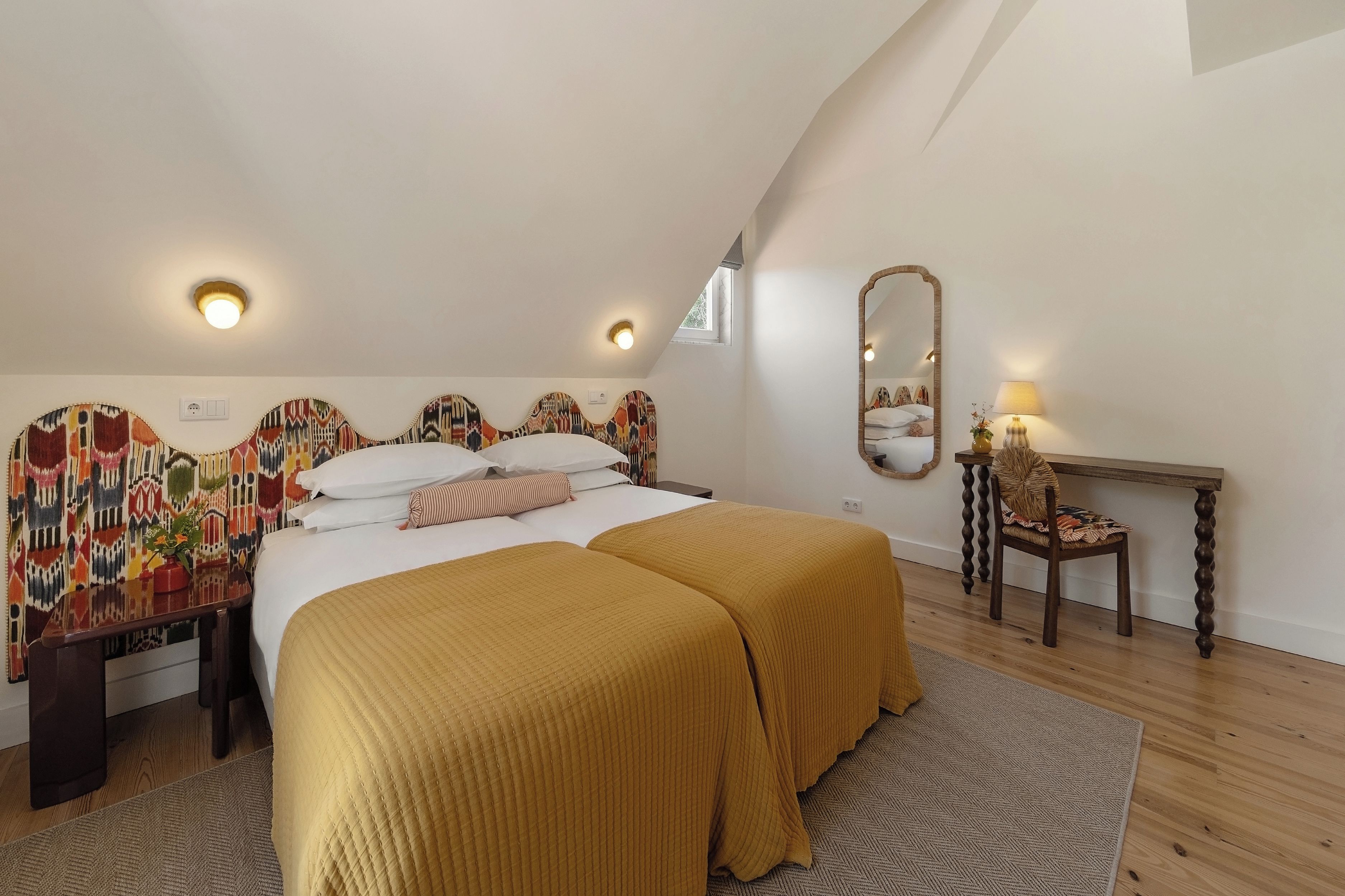 A bedroom with a bed, two bedside tables, a mirror, and a window.