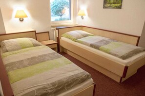 A double room with two beds, each with a pillow and a nightstand. There are wall-mounted lamps and a window with a view of trees. - Comfort "Am Spreewaldfliess" (Schlepzig)