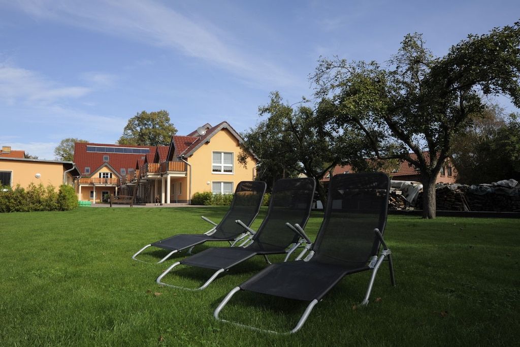 A grassy area with two black lounge chairs and a building with a red roof in the background.