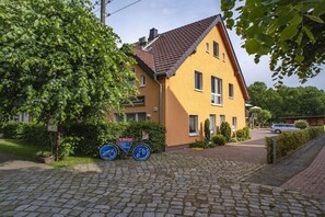 A yellow building with a sloped roof, a cobblestone driveway, and a sign indicating a bike rental service. - Comfort "Am Spreewaldfliess" (Schlepzig)